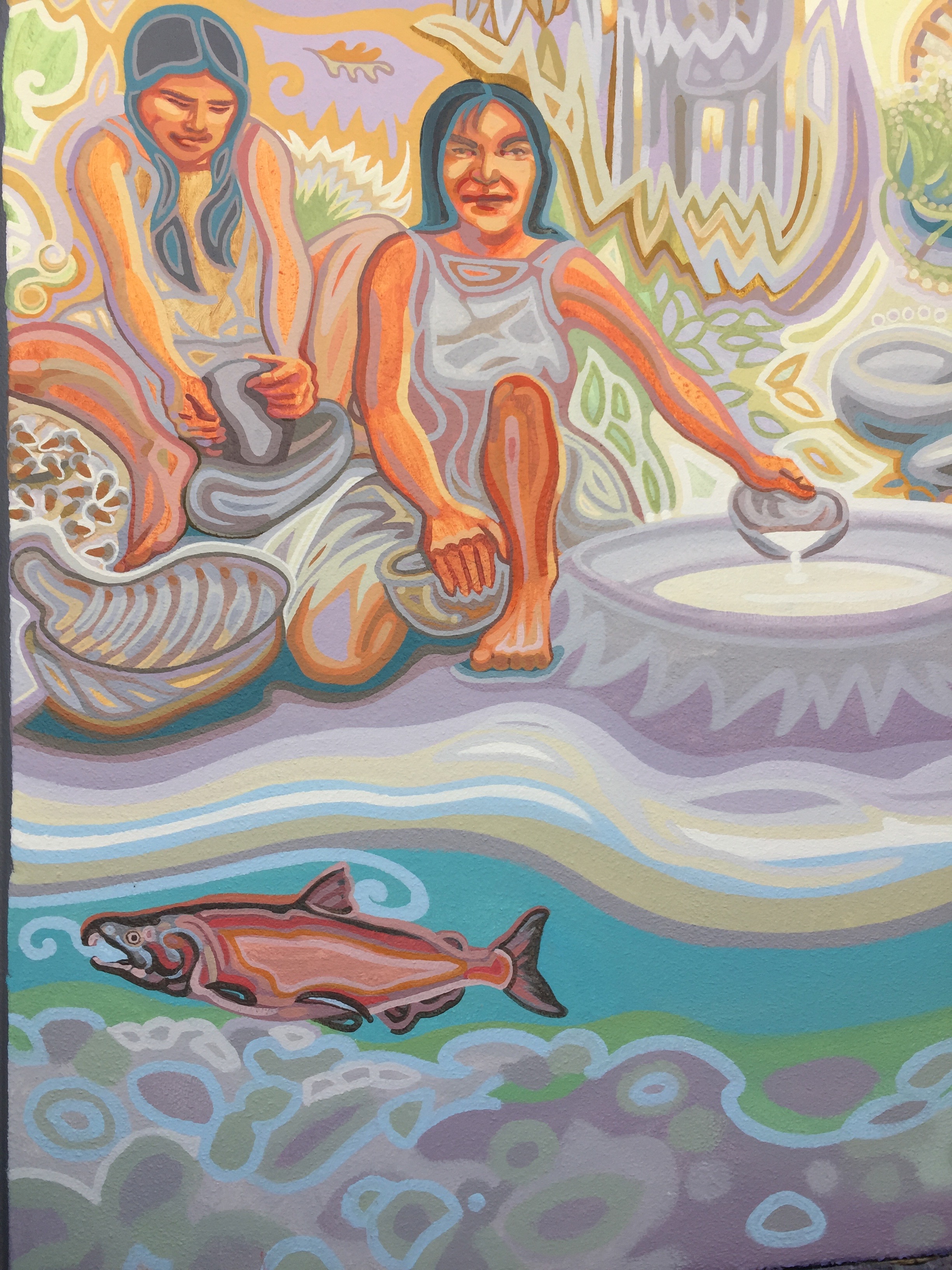A salmon in the stream in front of two Native women processing acorns.