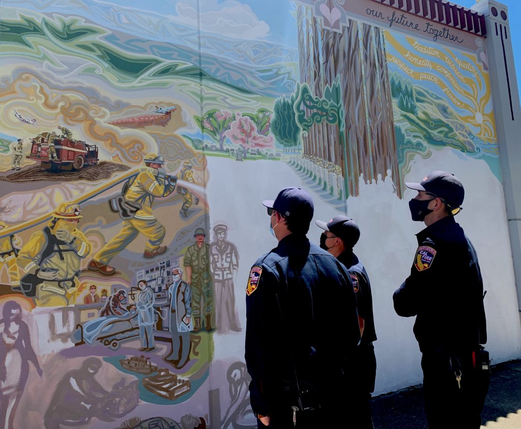 CalFire members looking at mural painting of firefighters