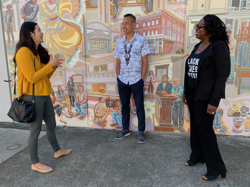 Asian, Native, and African American members of the community interacting in front of the mural